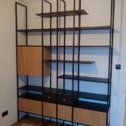 Regal z czarną metalową konstrukcją i drewnianymi elementami w odcieniach brązu, zlokalizowany we Wrocławiu, na podłodze widoczne zabezpieczenia.