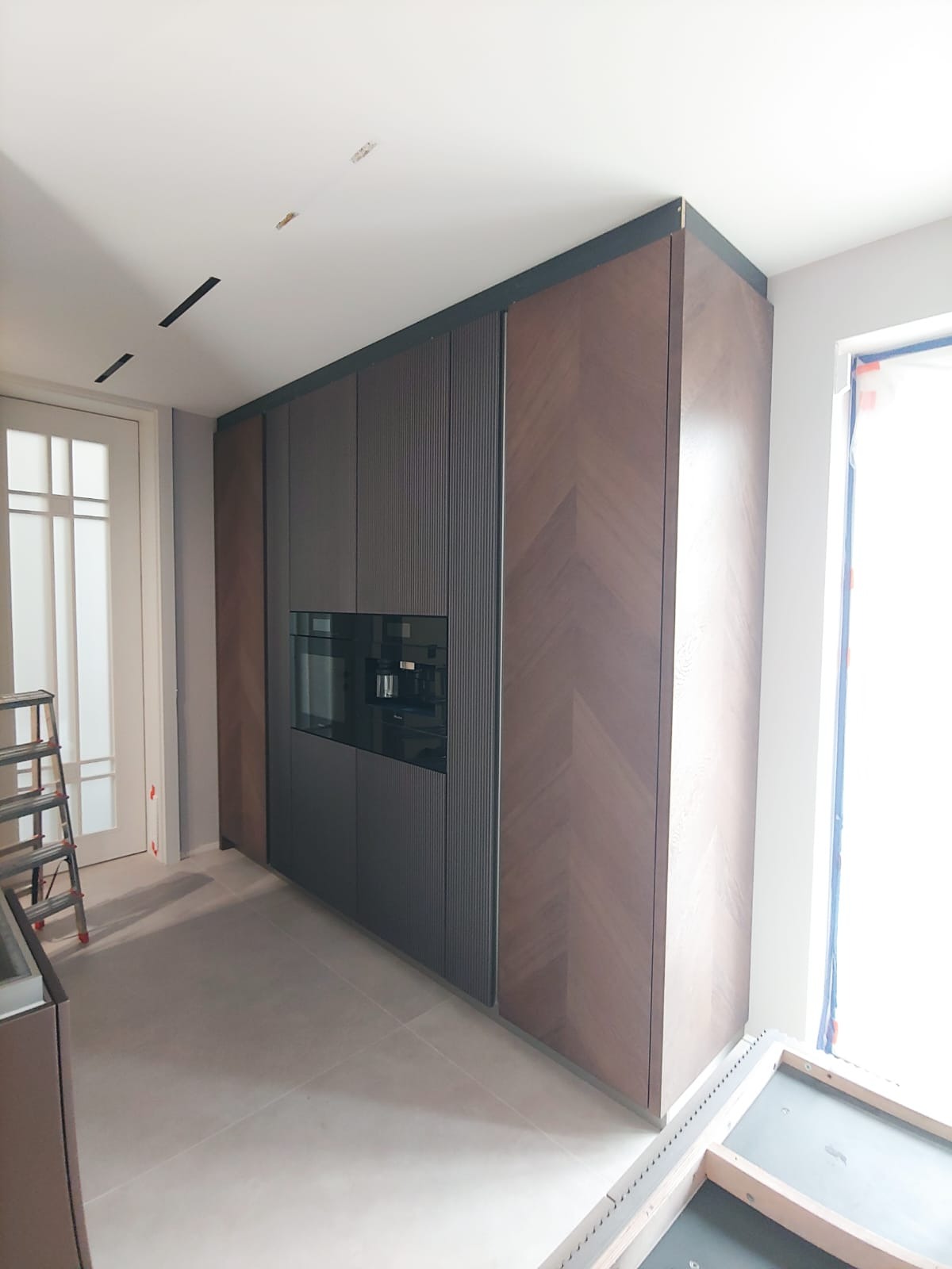 Nowoczesna zabudowa kuchenna z ciemnego drewna z wbudowanym sprzętem AGD we Wrocławiu, widoczne elementy wykończeniowe podłogi i drabina malarska.