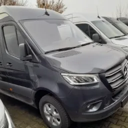 Rząd zaparkowanych szarych busów Mercedes Sprinter, widok z przodu, z anteną na dachu pierwszego pojazdu.