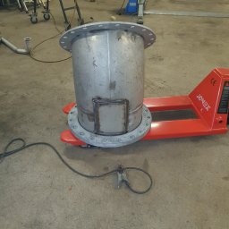 KIERTOM - Metalowy cylinder z przyspawaną klapą i kołnierzami na wózku paletowym, widoczny przewód spawalniczy na betonowej podłodze warsztatu.