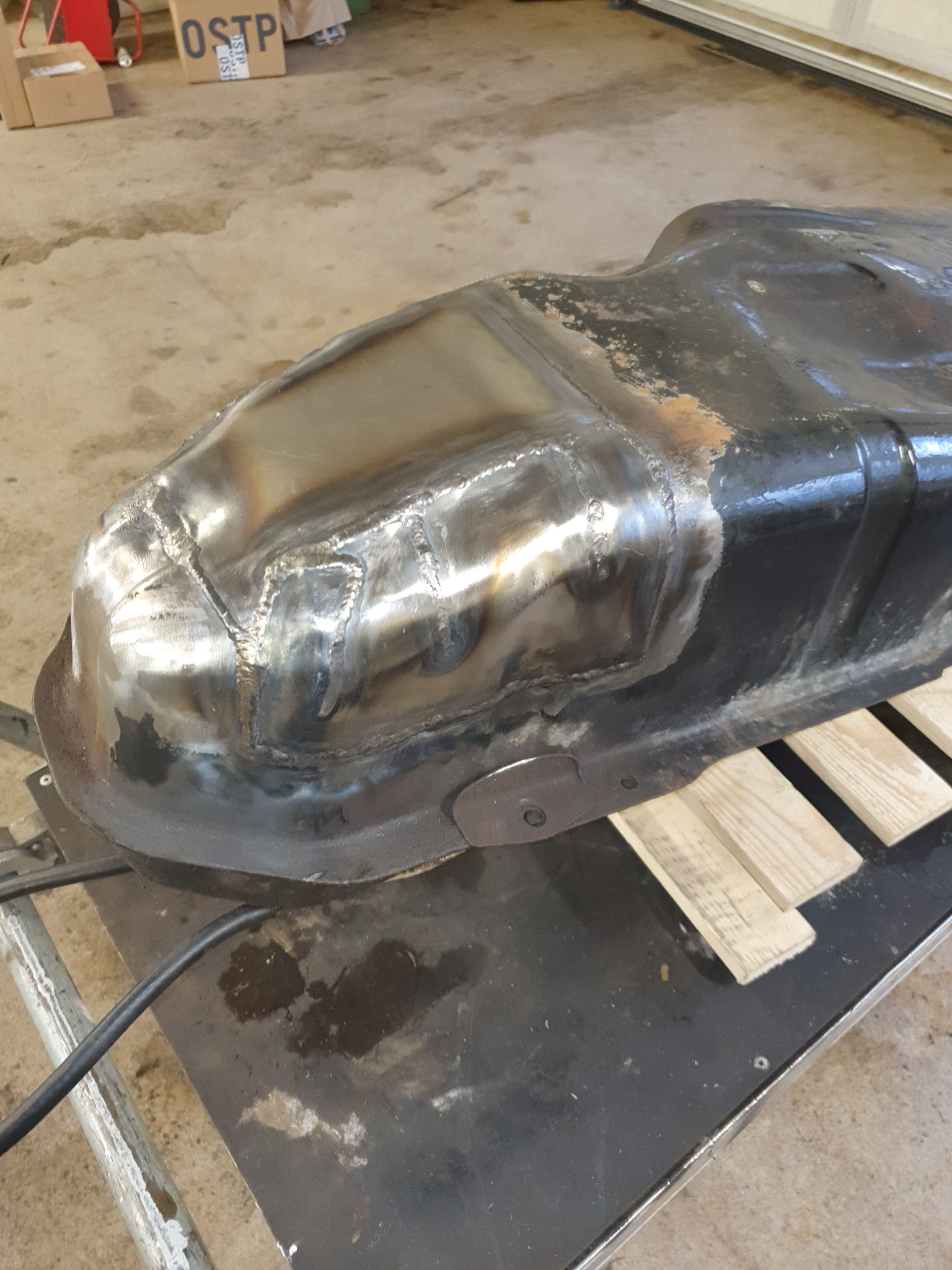 Naprawiony, spawany zbiornik paliwa na stole warsztatowym z widocznymi śladami spawania i naprawy.