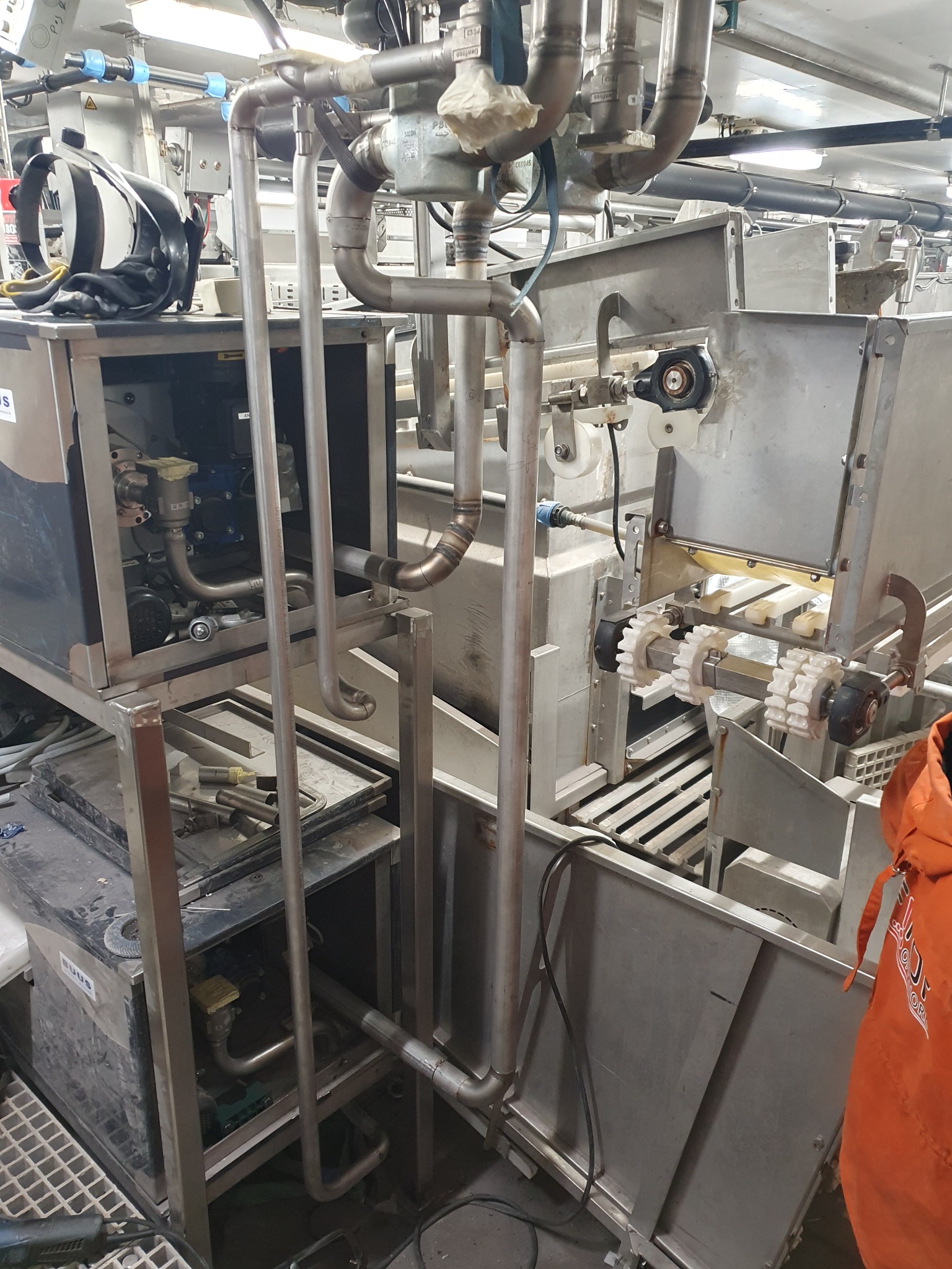 Zdjęcie przedstawia skomplikowaną instalację przemysłową ze stali nierdzewnej, z licznymi rurami, zaworami i elementami mechanicznymi. Widoczne są również fragmenty urządzeń sterujących i obudów.