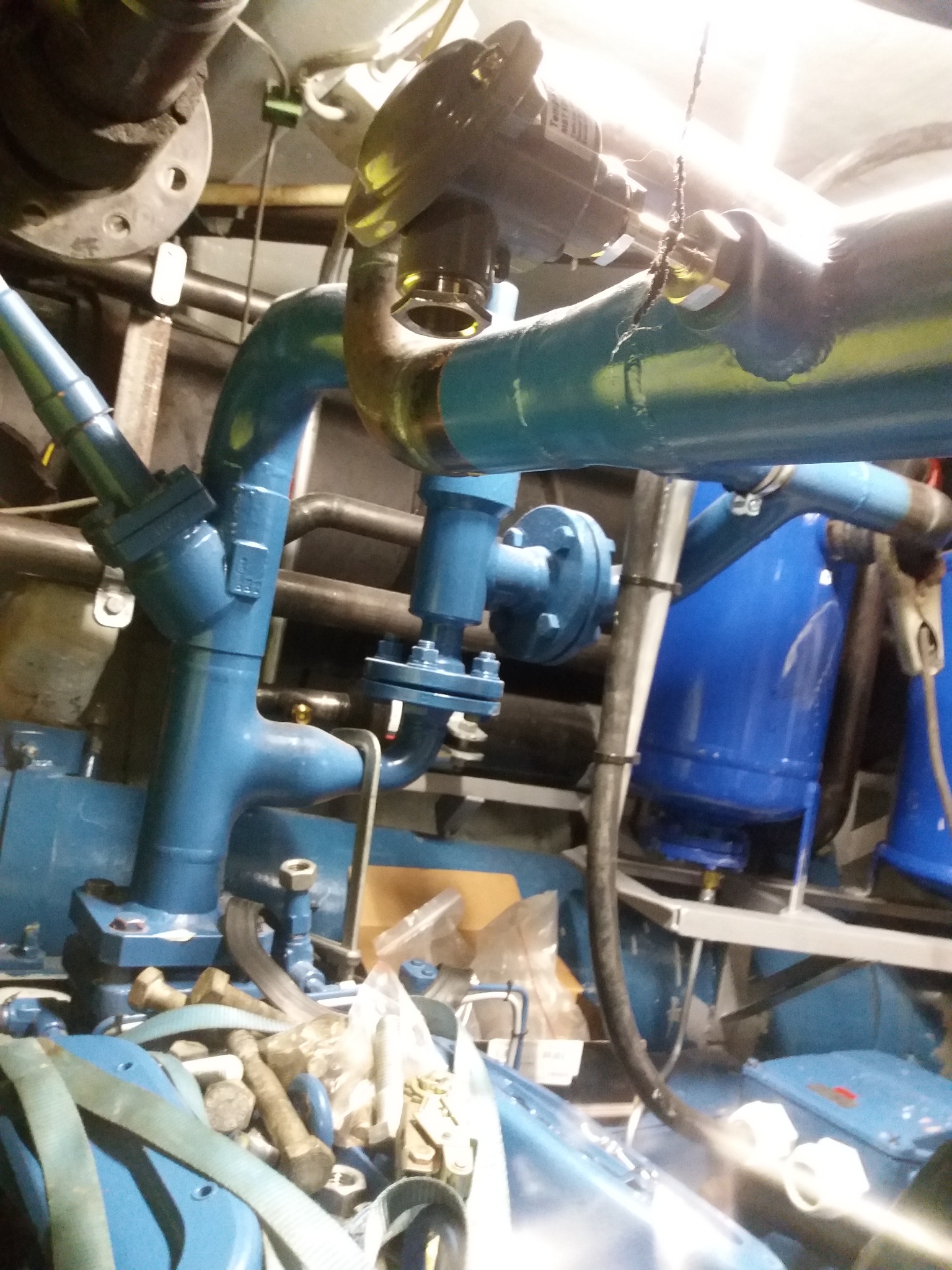 Niebieskie rury i zawory przemysłowe, widoczne ślady spawania i montażu, elementy przytwierdzone do konstrukcji, w tle zbiorniki ciśnieniowe.