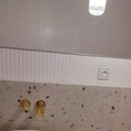 Wykończenia Andrzej Kobylański - Nowoczesna łazienka: beżowy blat lastryko, złota armatura, owalne lustro z podświetleniem LED i widocznym odbiciem osoby. Minimalistyczne gniazdka elektryczne.