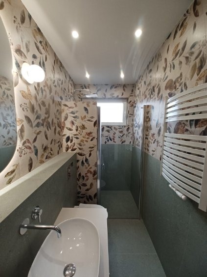 Ukończona łazienka z umywalką, grzejnikiem i kabiną prysznicową, wykończona w motywie liści. Widok z góry na całe pomieszczenie.