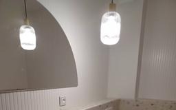 Nowoczesna łazienka z białymi ścianami, oświetleniem punktowym i lustrem w kształcie łuku. Umywalka z blatem z lastryko. Minimalistyczny design.