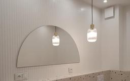 Biała łazienka z półokrągłym lustrem i wiszącą lampą. Ściana z delikatną fakturą, blat z lastryko. Minimalistyczny design, nowoczesne oświetlenie.