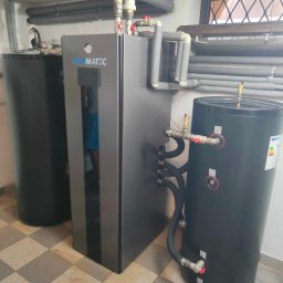 Elektrowniesloneczne.tech - Instalacja z zbiornikami akumulacyjnymi i rurami w izolacji, widoczne logo Thermatec na szarym urządzeniu, posadzka w szachownicę.