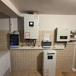 Elektrowniesloneczne.tech - Kompletna instalacja fotowoltaiczna w pomieszczeniu z beżowymi płytkami, widoczne inwertery, rozdzielnice i magazyn energii. Elementy połączone przewodami.