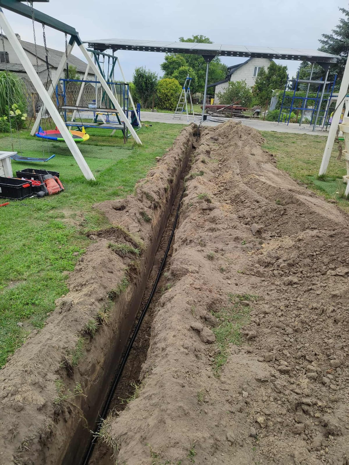 Wykop pod instalację w Skierniewicach. W tle konstrukcja pod panele. Widoczny kabel w ziemi, narzędzia obok. Wykopana ziemia tworzy wał po obu stronach.