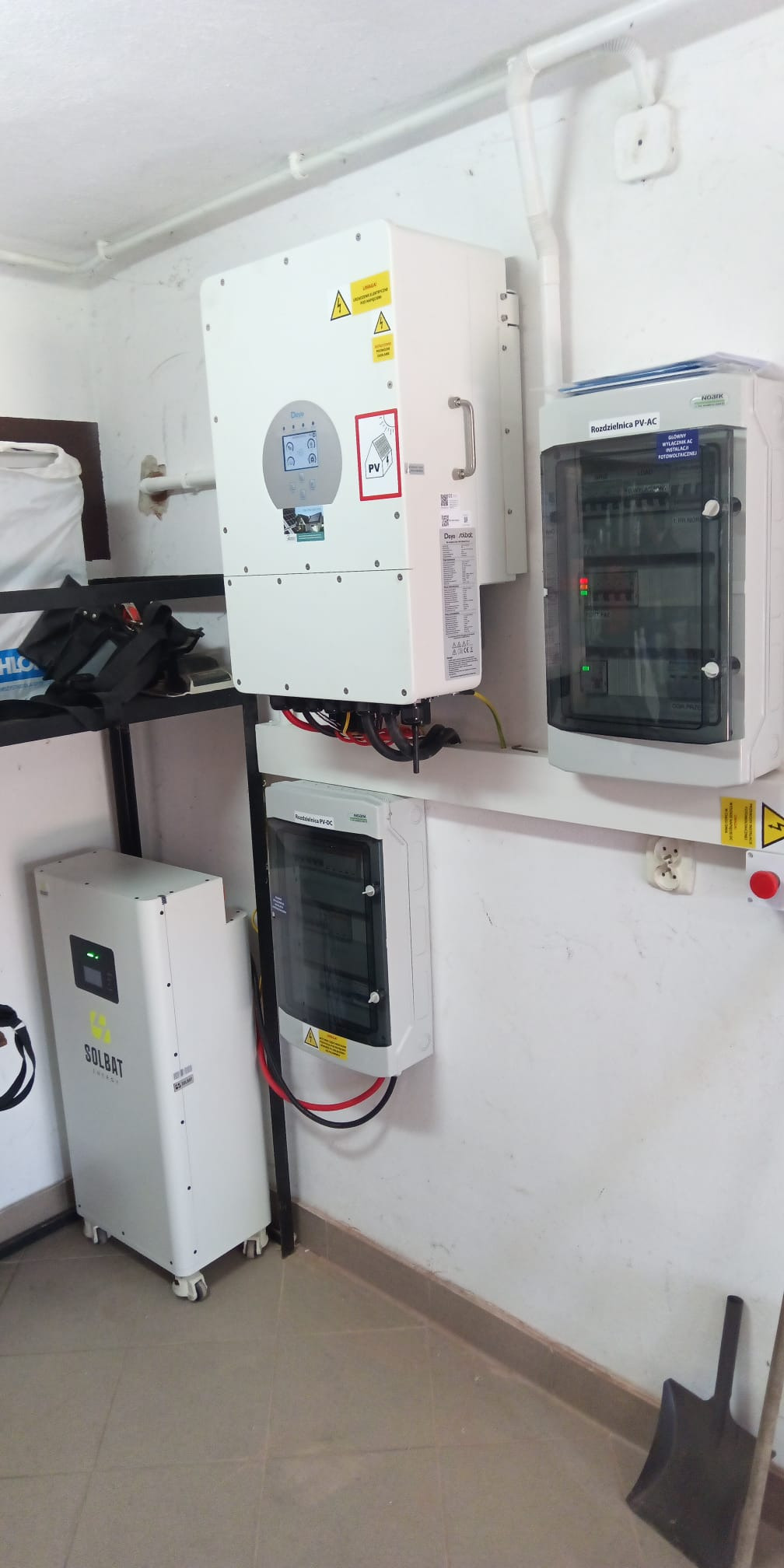 Kompletna instalacja fotowoltaiczna w pomieszczeniu: inwerter Deye, bateria Solbat, rozdzielnice PV-AC i PV-DC. Widoczne kable i elementy montażowe.