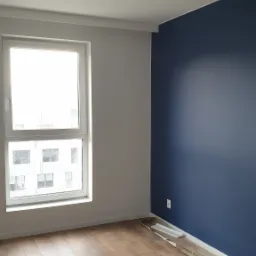 Pomalowane na granatowo ściana w pokoju z drewnianą podłogą i białym oknem, widoczne panele przypodłogowe przy ścianie.
