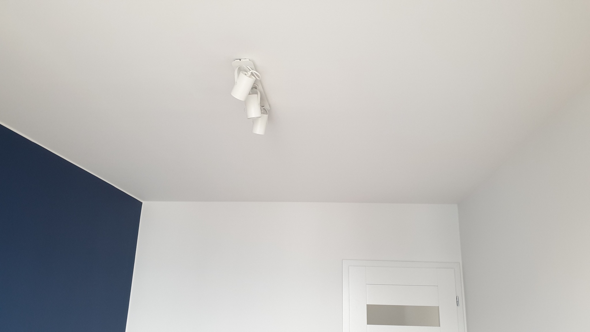 Wnętrze w Brzeszczach po remoncie: biały sufit z reflektorami, ściana w odcieniu granatu i białe ściany z drzwiami.