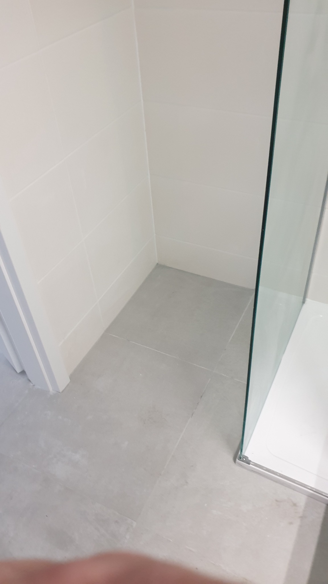 Fragment wykończonej łazienki z szarymi płytkami podłogowymi, białymi płytkami ściennymi i fragmentem szklanej kabiny prysznicowej z chromowanymi okuciami