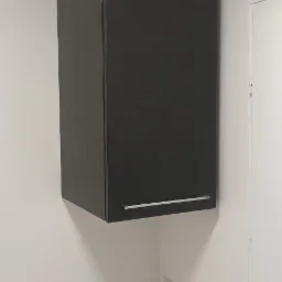 Ciemnoszara szafka wisząca z metalowym uchwytem na tle białej ściany z widocznymi otworami i gniazdkiem elektrycznym.