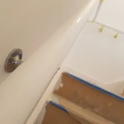 Świeżo pomalowana biała poręcz schodowa z metalowymi uchwytami, widoczne zabezpieczenia taśmą malarską na schodach.