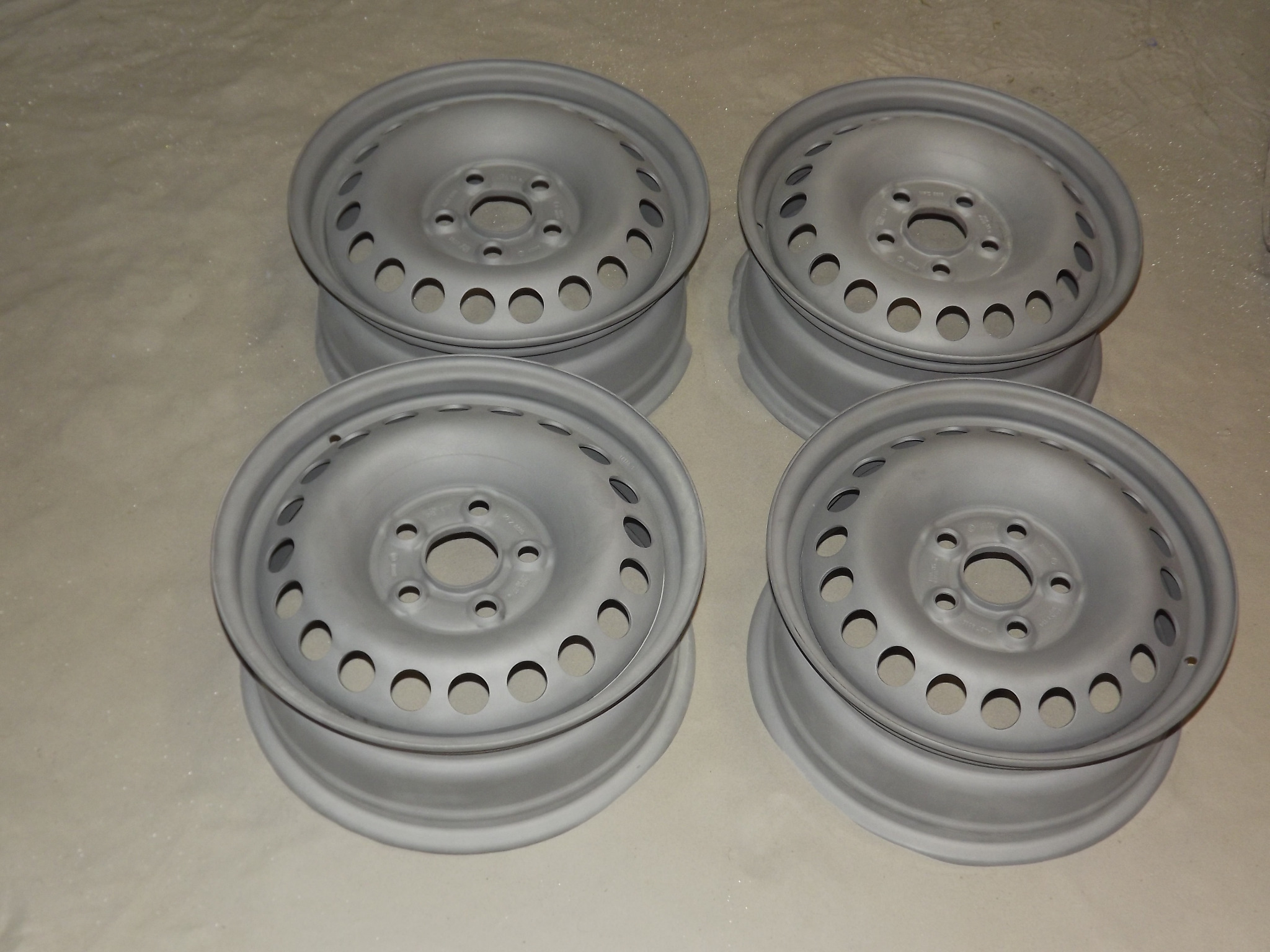 Cztery stalowe felgi samochodowe po piaskowaniu, przygotowane do malowania proszkowego, widoczne otwory wentylacyjne i centralny otwór montażowy.
