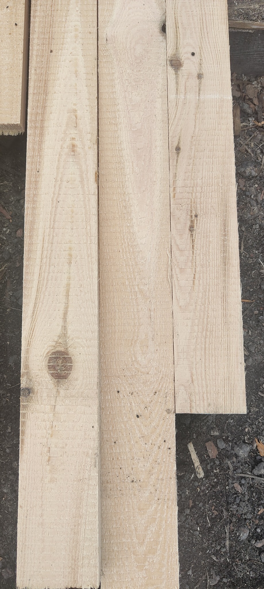 Surowe deski z widocznymi słojami i sękami, leżące na ziemi.