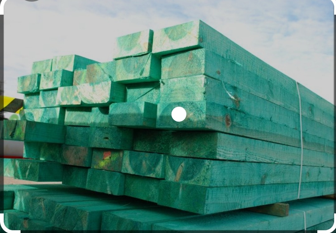 Stos impregnowanej, zielonej tarcicy budowlanej ułożonej w regularny stos, widoczne słoje drewna i wiązania sznurkiem.