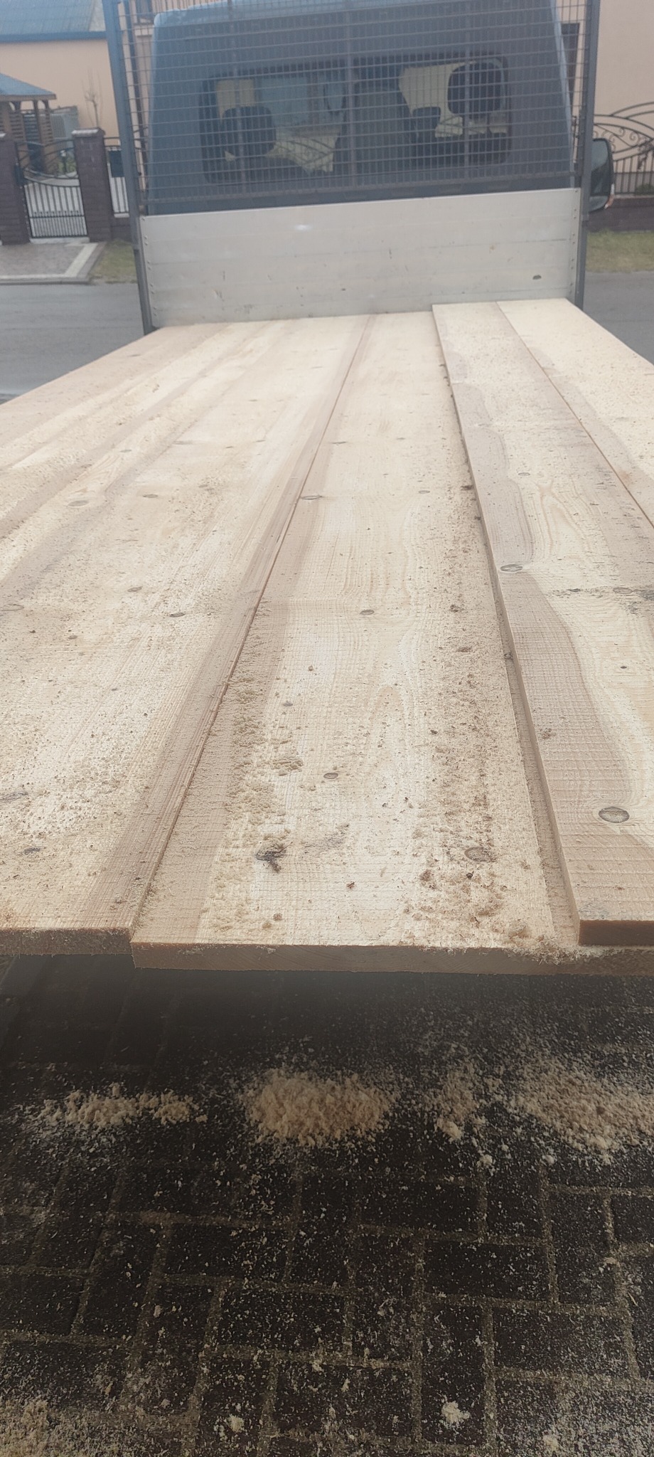 Świeżo przetarte deski ułożone w skrzyni samochodu dostawczego, pokryte drobnymi wiórami i pyłem drzewnym.