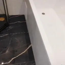 Biała wanna z złotą armaturą na tle marmurowych płytek w odcieniach czerni i bieli. Nowoczesna łazienka po remoncie z eleganckimi detalami.