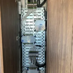 Rozdzielnica elektryczna z licznymi kablami i modułami, zamontowana w szafce z drewnianymi drzwiami.