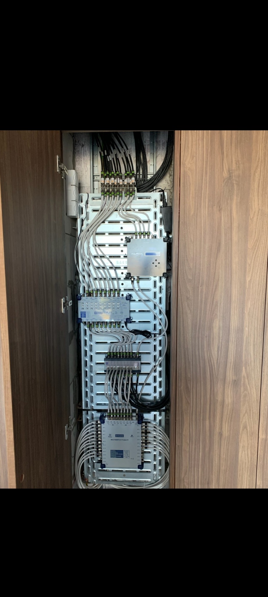 Rozdzielnica elektryczna z licznymi kablami i modułami, zamontowana w szafce z drewnianymi drzwiami.