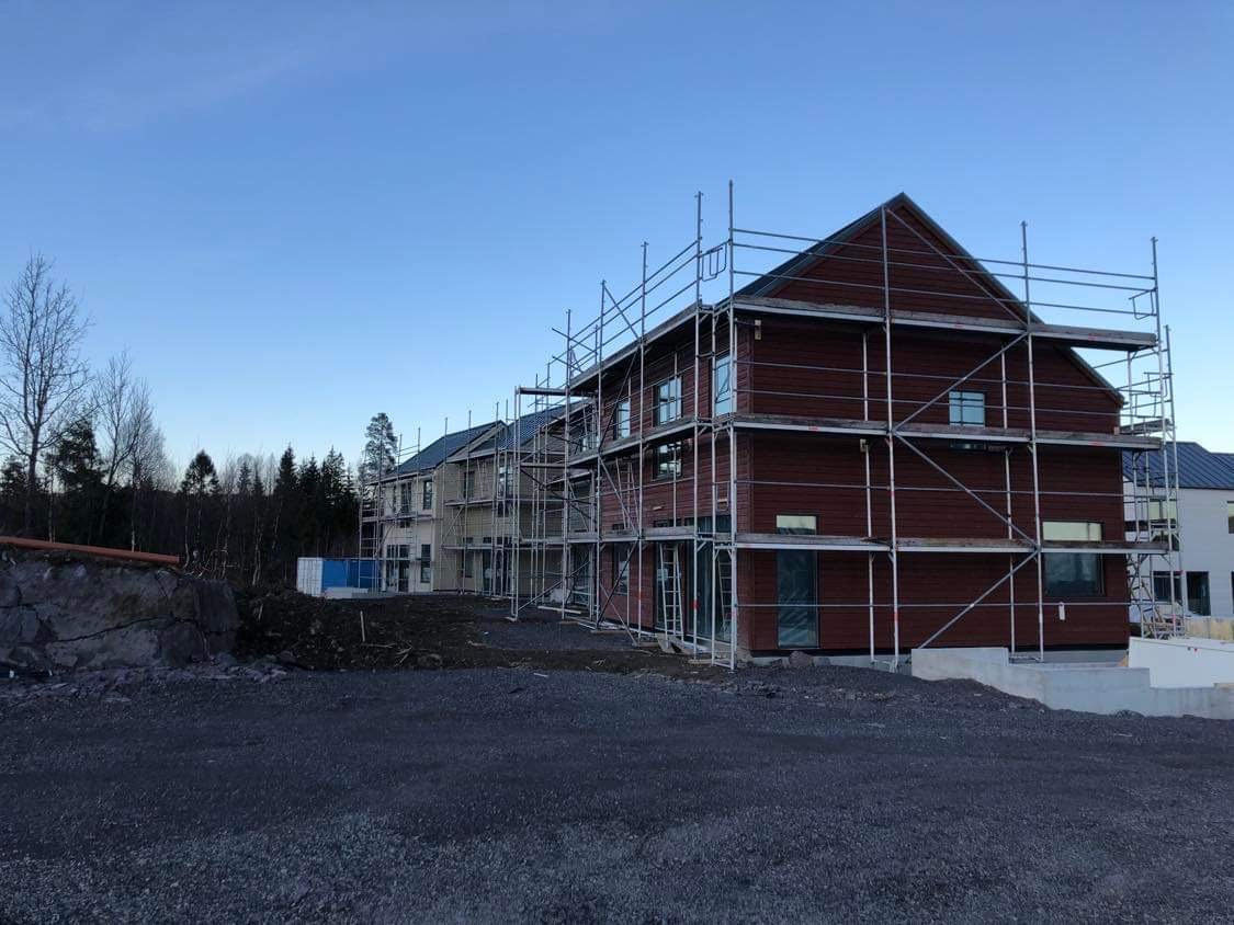 Budynek w trakcie budowy, otoczony rusztowaniami, z widocznymi elementami konstrukcji drewnianej i przygotowanym terenem.