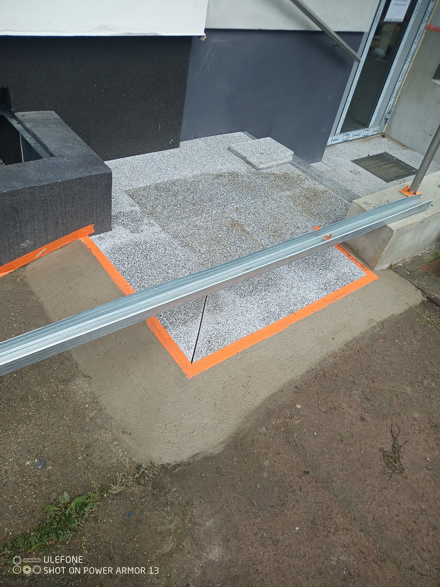 Przygotowanie podłoża pod schody wejściowe z żywicy epoksydowej, widoczne profile aluminiowe i pomarańczowa taśma wyznaczająca obszar roboczy.