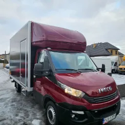 Czerwony samochód dostawczy Iveco z zabudową kontenerową i aluminiowymi drzwiami, zaparkowany na mokrym, częściowo ośnieżonym placu.