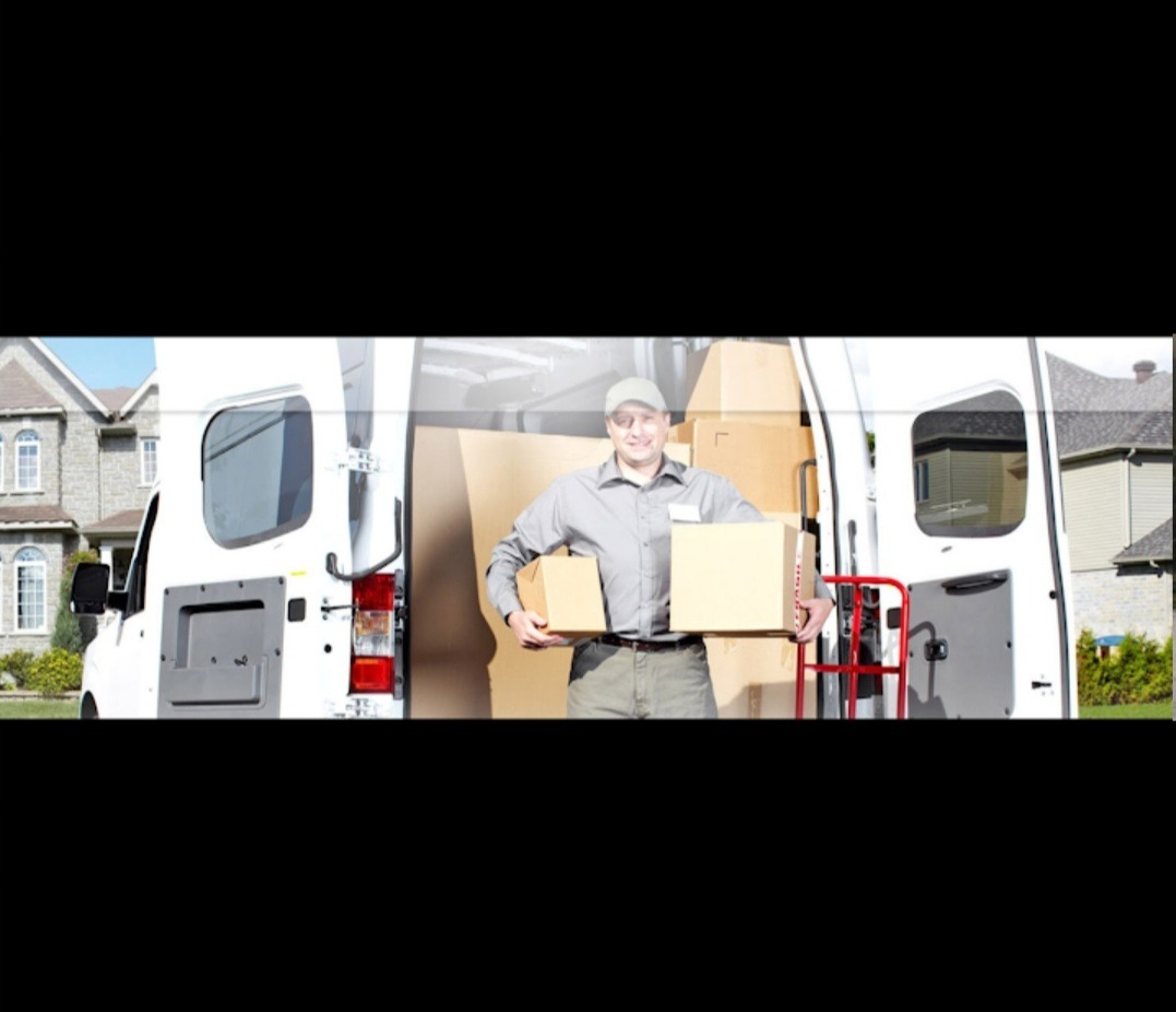 Uśmiechnięty mężczyzna w szarej koszuli i czapce trzyma dwa kartony przed otwartym tyłem białego vana wypełnionego pudłami, z domem jednorodzinnym w tle.