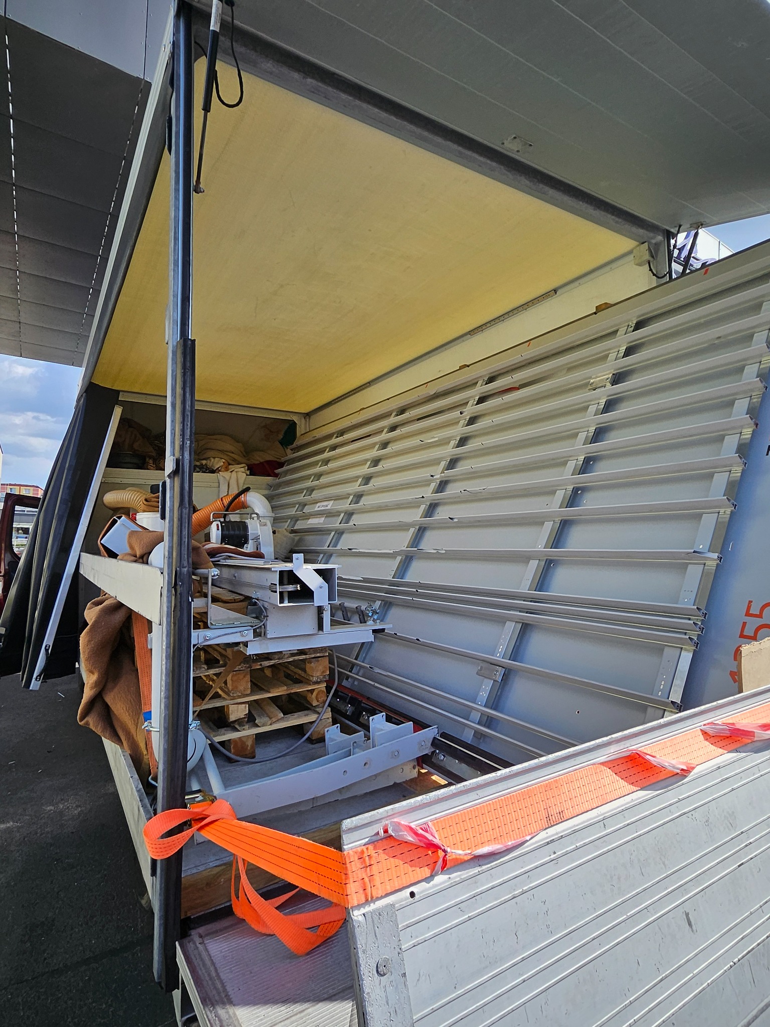 Wnętrze skrzyni ładunkowej z zabezpieczonymi paletami, urządzeniami i pomarańczowymi pasami mocującymi, widok z zewnątrz skrzyni.