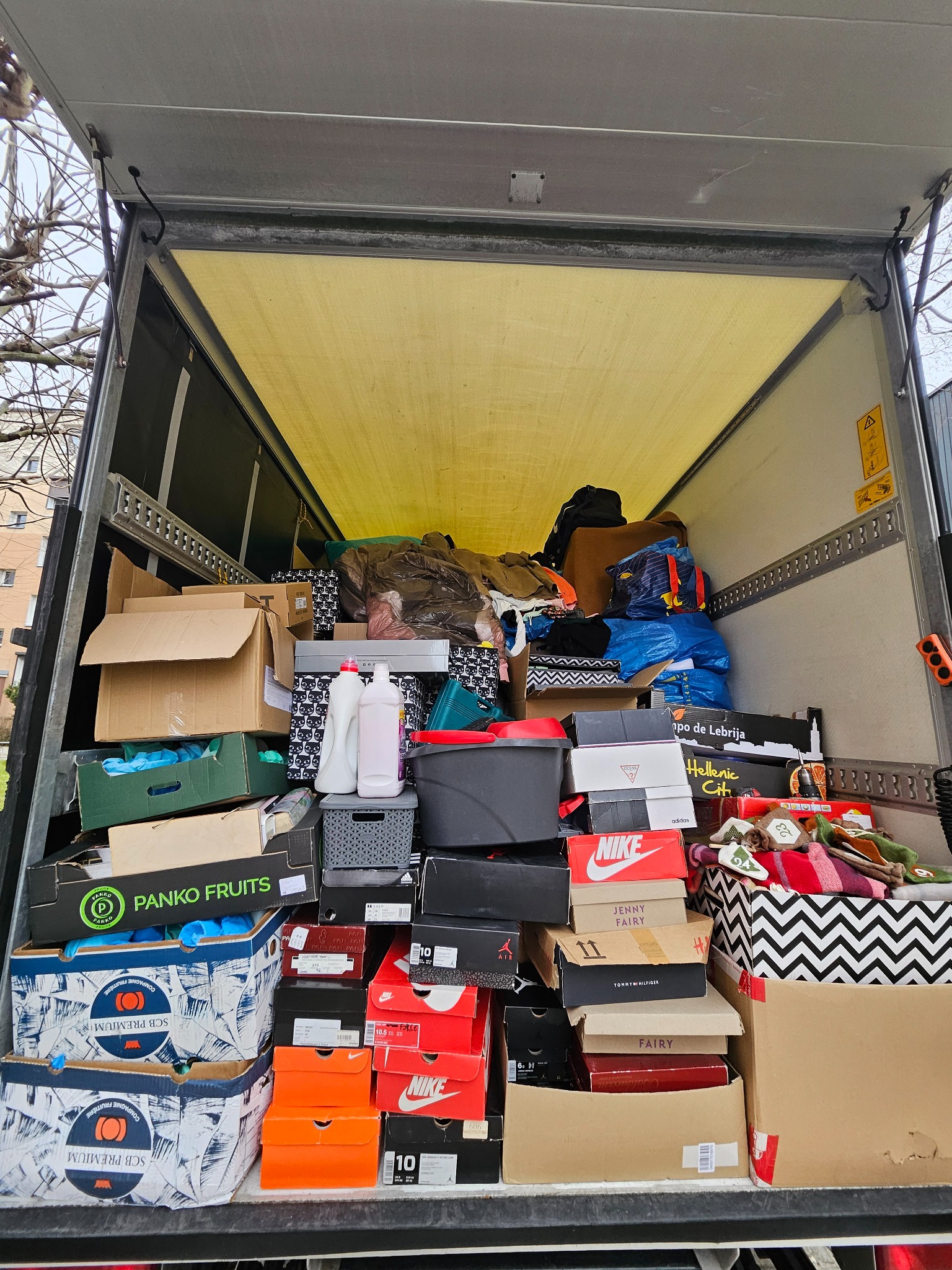 Wnętrze samochodu dostawczego wypełnione po brzegi kartonami, pudełkami po butach (Nike, Adidas, Tommy Hilfiger, Jenny Fairy), pojemnikami i workami podczas przeprowadzki, widok z tyłu pojazdu.