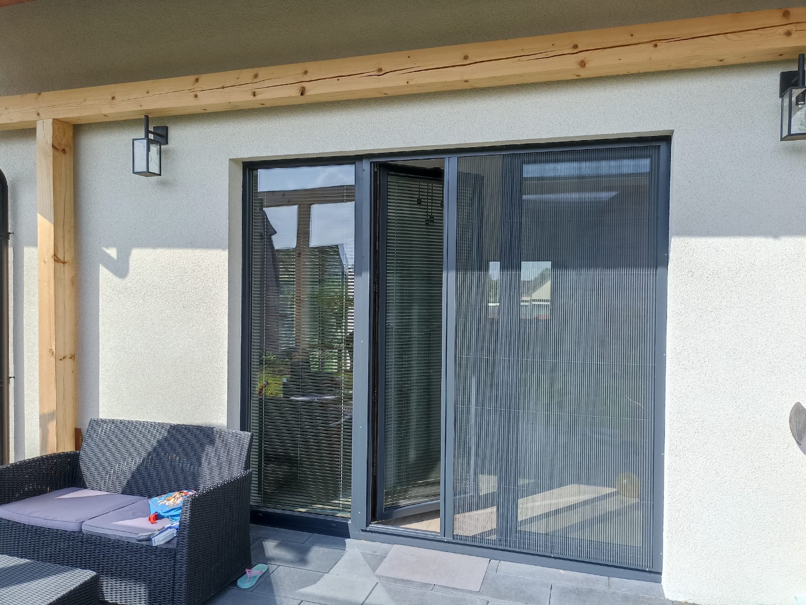 Zewnętrzne przesuwne drzwi tarasowe z zamontowaną plisowaną siatką przeciw owadom, widok z zewnątrz tarasu.