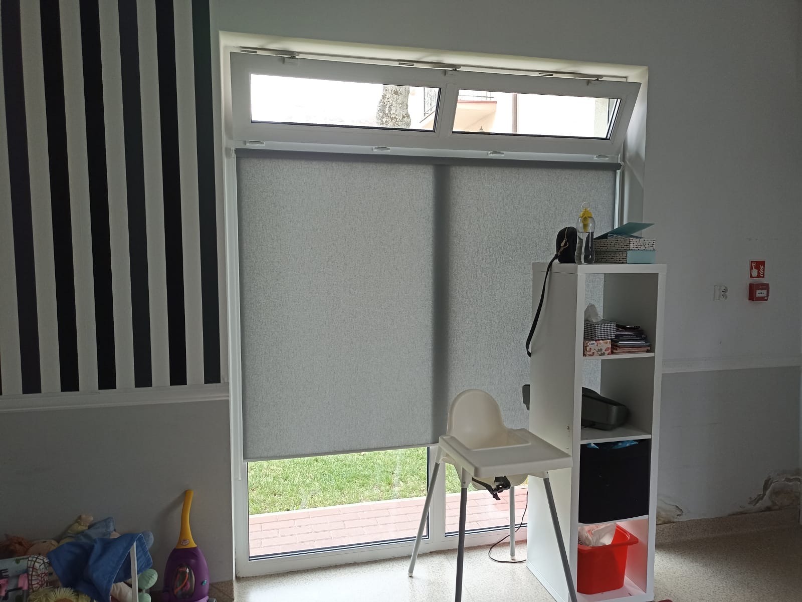 Zasłonięte szare okno z widokiem na zewnątrz, w pokoju dziecięcym z czarno-białą tapetą i krzesełkiem do karmienia.