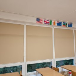 Firma AMS - Beżowe rolety wewnętrzne w sali lekcyjnej w Radomsku, z widocznymi flagami różnych państw nad oknami.