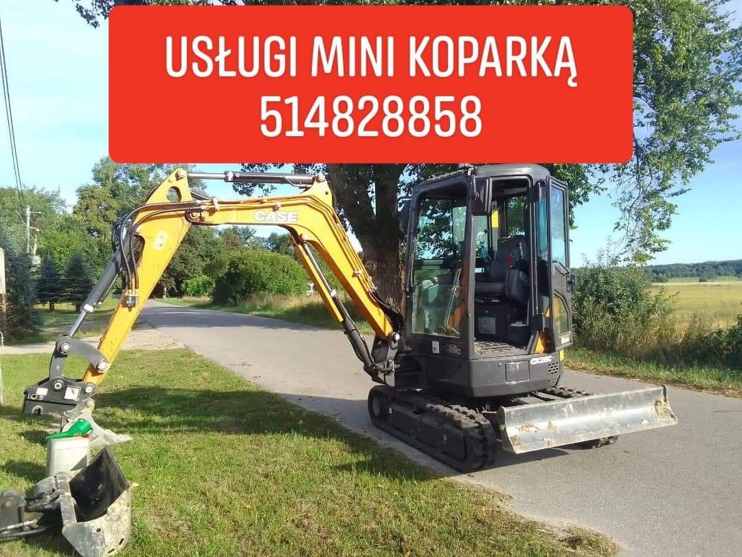 Żółto-czarna mini koparka CASE stoi na poboczu asfaltowej drogi, z przodu widoczny osprzęt, w tle łąka i drzewa, na górze czerwony baner z napisem 'Usługi mini koparką' i numerem telefonu.