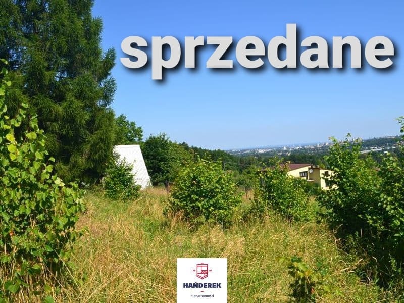 Działka z widokiem na miasto, oznaczona napisem 'sprzedane' i logo agencji nieruchomości w rogu.