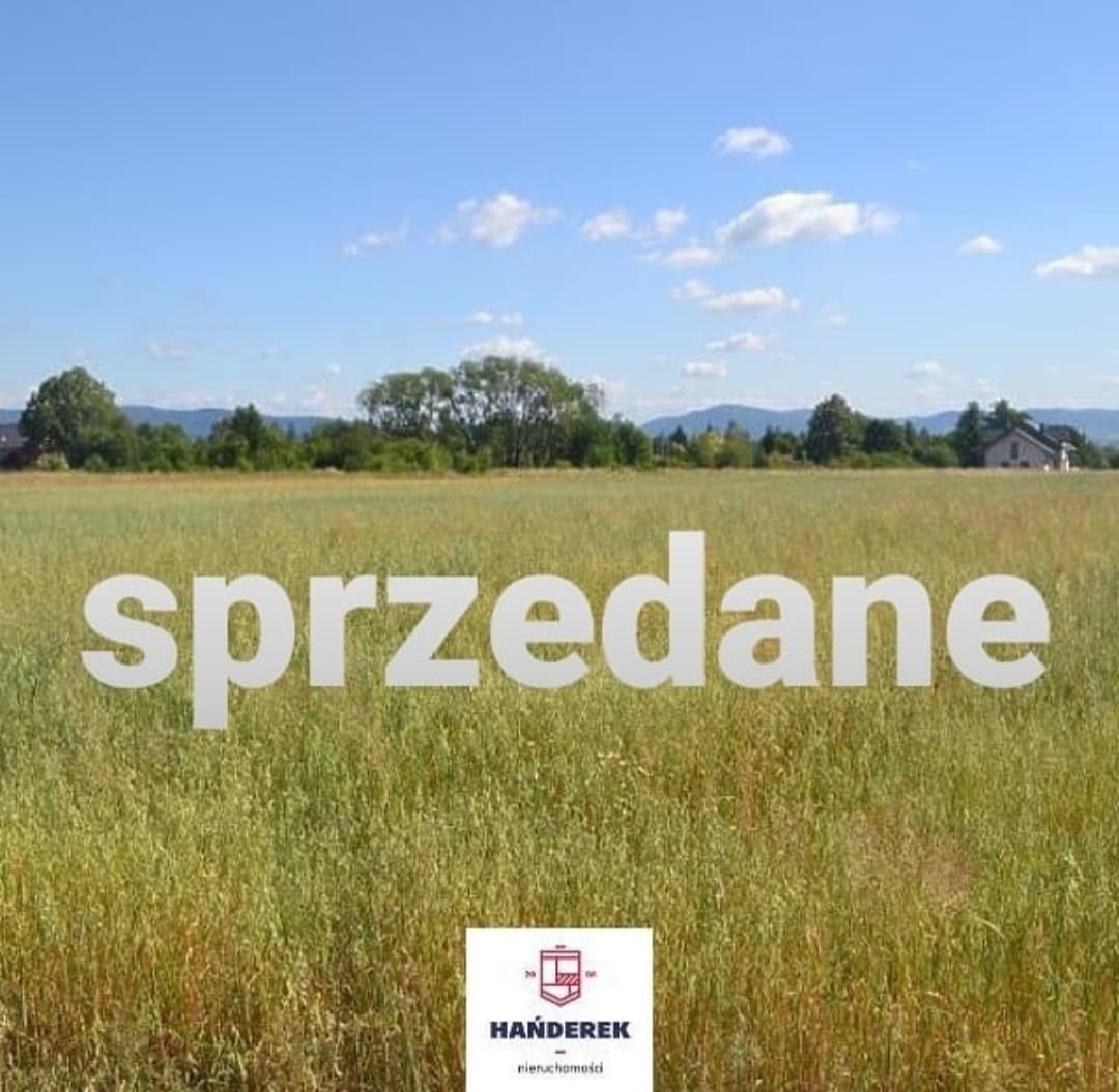 Pole z wysoką trawą pod błękitnym niebem, w tle las i dom, na pierwszym planie napis 'sprzedane' i logo agencji nieruchomości Hańderek.