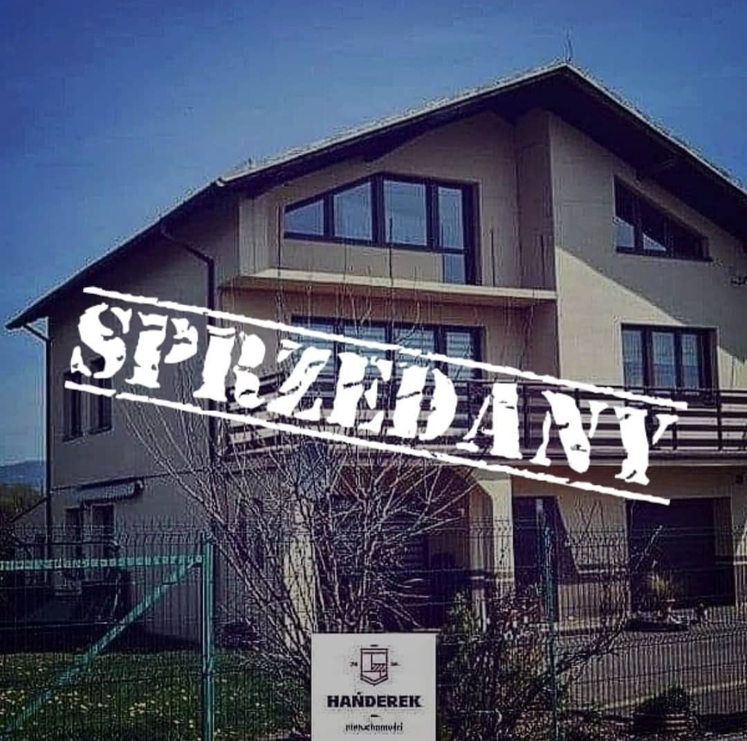 Dwupiętrowy dom z balkonem, na zdjęciu nałożony napis 'SPRZEDANY', w tle błękitne niebo, z przodu siatka ogrodzeniowa i logo agencji nieruchomości.