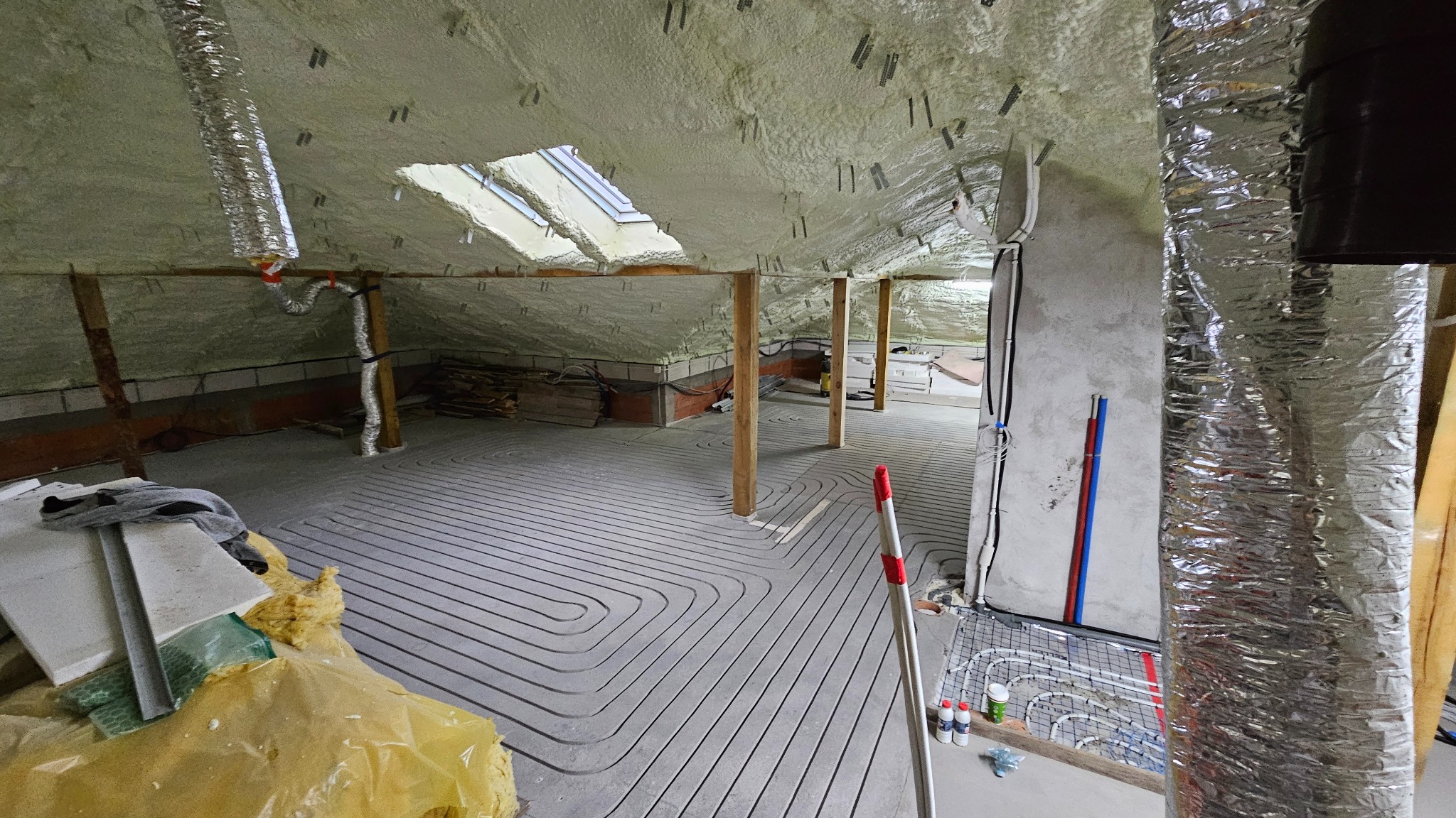 Poddasze po ociepleniu pianą PUR i instalacji ogrzewania podłogowego. Widoczne rury grzewcze ułożone w charakterystyczny wzór, okno dachowe i elementy konstrukcji.