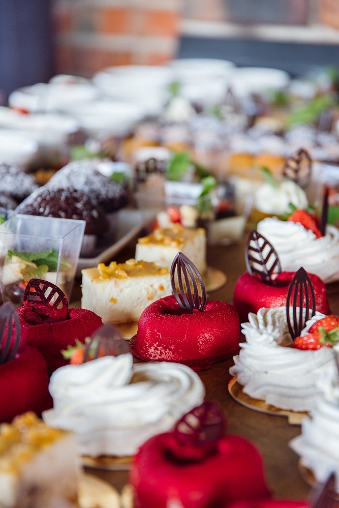 Różnorodne, eleganckie desery na stole: czerwone serca z aksamitną glazurą, białe babeczki z kremem, ciasta z owocami i czekoladowe muffinki posypane cukrem pudrem. Dekoracyjne elementy z czekolady...