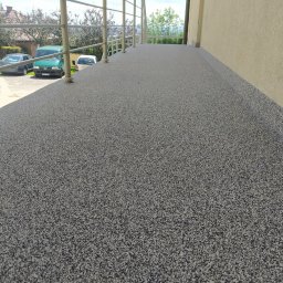 AM-system usługi budowlane - Szara, drobnoziarnista posadzka żywiczna na balkonie z metalową balustradą, widok z niskiej perspektywy, w tle zaparkowane samochody i zieleń.