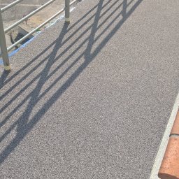 AM-system usługi budowlane - Nowa, szara, żywiczna nawierzchnia balkonu w Opolu z metalową barierką, rzucająca cienie. W tle widoczne maszyny budowlane.