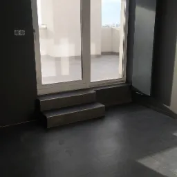 Nowoczesne wnętrze z ciemną podłogą z płytek, dwuskrzydłowymi drzwiami balkonowymi z niskim progiem i schodkami w kolorze podłogi oraz grzejnikiem panelowym na ścianie.