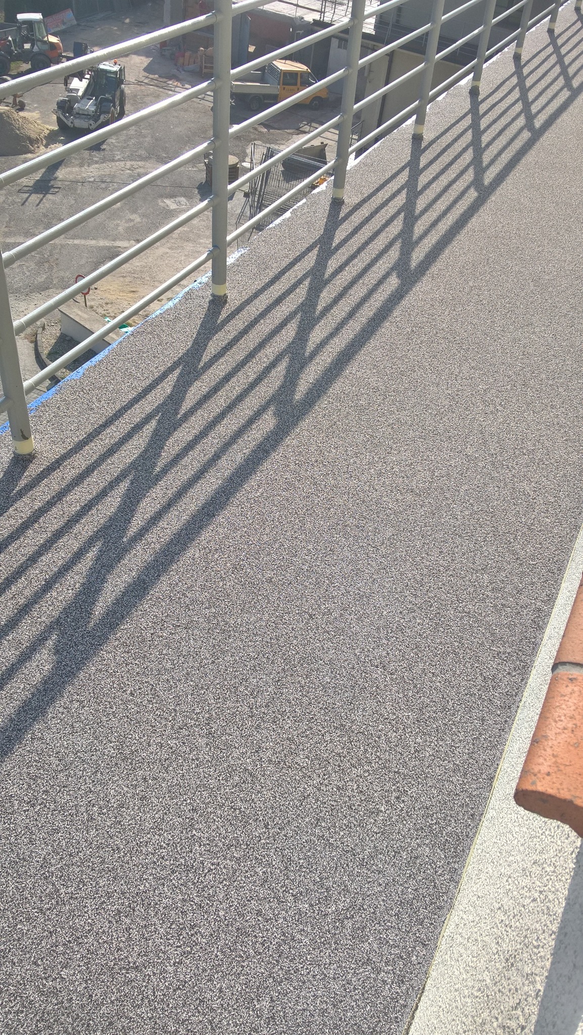Nowa, szara, żywiczna nawierzchnia balkonu w Opolu z metalową barierką, rzucająca cienie. W tle widoczne maszyny budowlane.