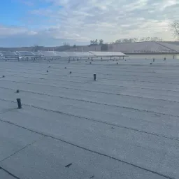 Płaski dach pokryty papą termozgrzewalną z widocznymi odpowietrznikami i panelami słonecznymi w tle, wykonany w technologii bezspoinowej.