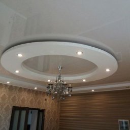 FORTUNA - Wykończone wnętrze z podwieszanym sufitem w kształcie okręgu z oświetleniem punktowym i ozdobnym żyrandolem, ściany wykończone tapetą i panelami ściennymi.