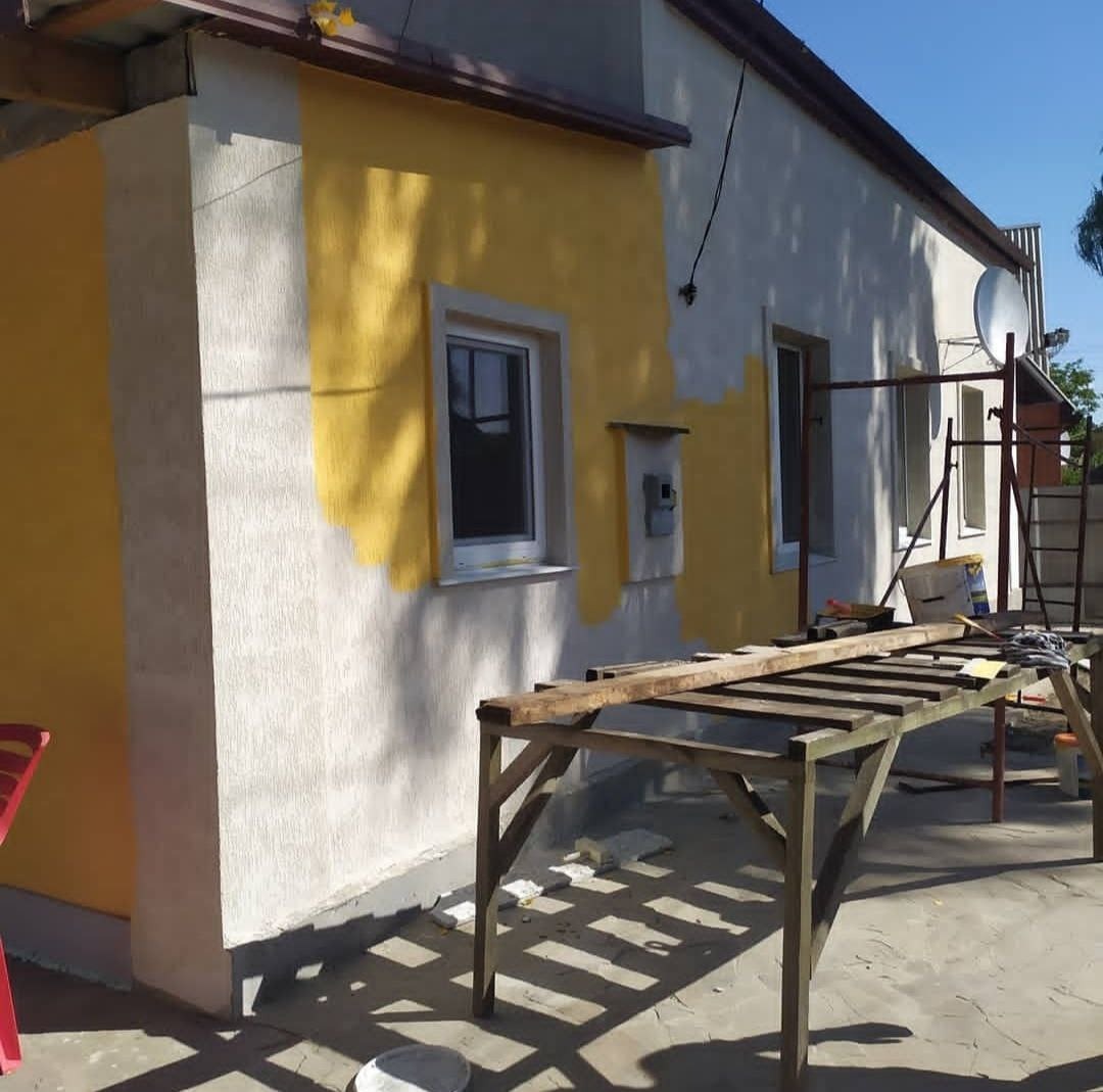 Malowanie elewacji domu jednorodzinnego na kolor żółty, widoczne rusztowanie i częściowo pomalowana ściana z oknem.