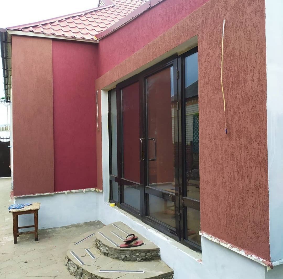 Dwukolorowa elewacja domu z oknami przesuwnymi, widoczne fragmenty nowej elewacji w odcieniach brązu i bordo, z detalami wykończeniowymi wokół okien i schodków wejściowych, na schodach leżą klapki.